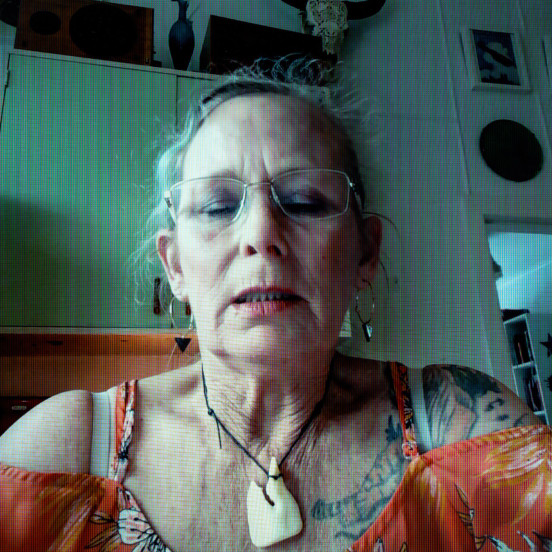 Photo of a woman sitting in kitchen with glasses on and bone carving necklace looking downwards