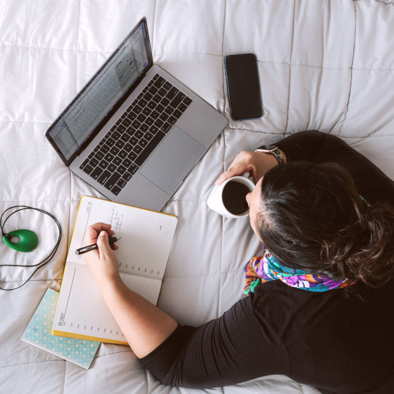 Aerial view of a woman lying down on a bed with devices and a cup of coffee