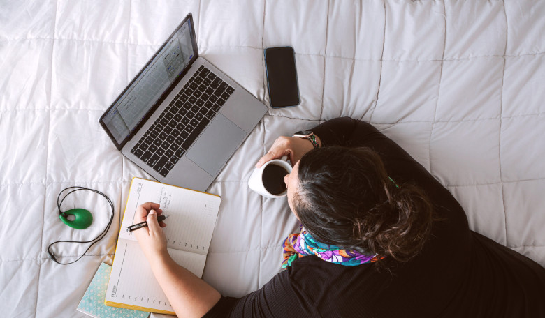 Aerial view of a woman lying down on a bed with devices and a cup of coffee