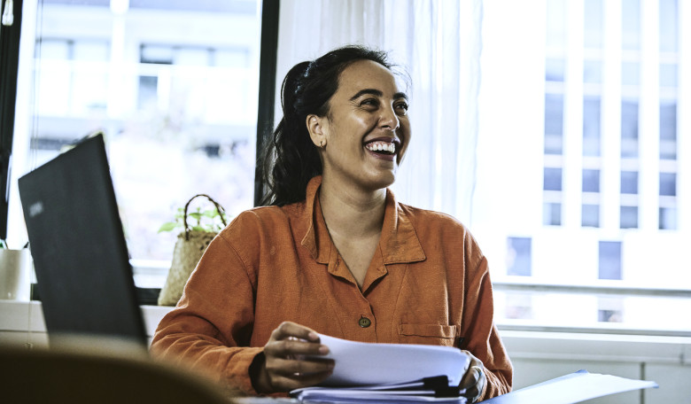 Woman sitting at desk holding documents and smiling