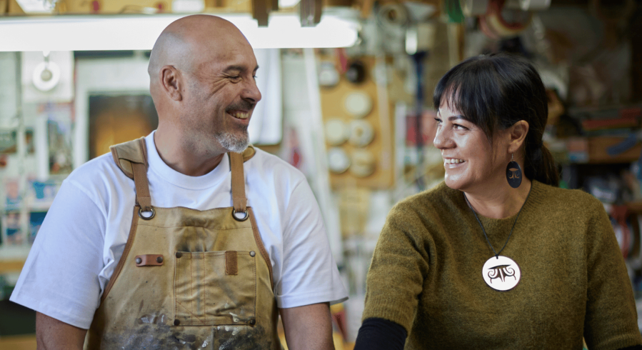 Photo of a man and a woman looking at each other and smiling, with a workshop in the background